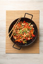 Shrimp stir fry with vegetables in wok and chopsticks on wooden table, top view