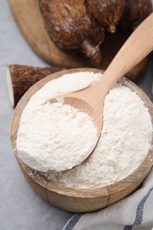 Photo of Wooden bowl and spoon with cassava flour on grey table, closeup