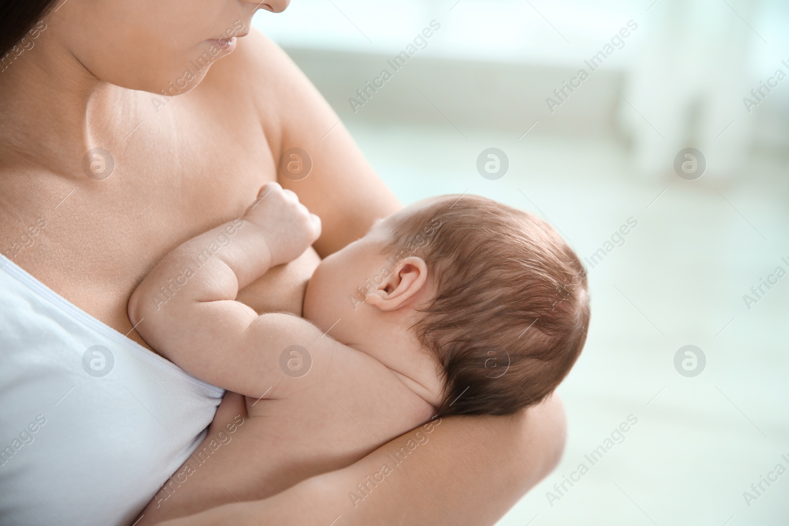 Photo of Young woman breastfeeding her baby on blurred background, closeup