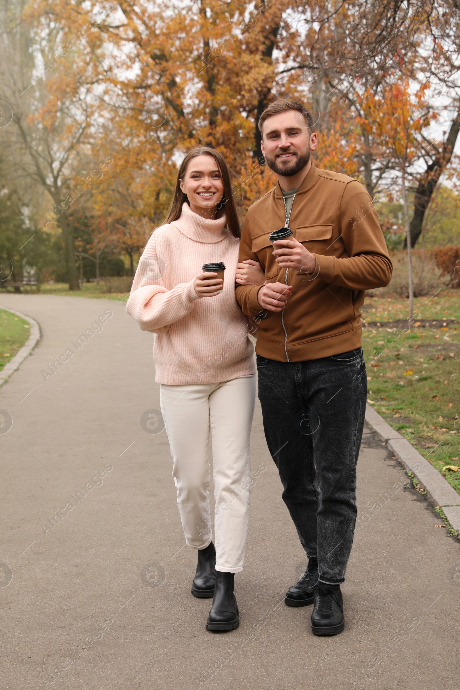 Photo of Happy couple wearing stylish clothes with cups of coffee in autumn park