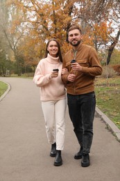 Photo of Happy couple wearing stylish clothes with cups of coffee in autumn park