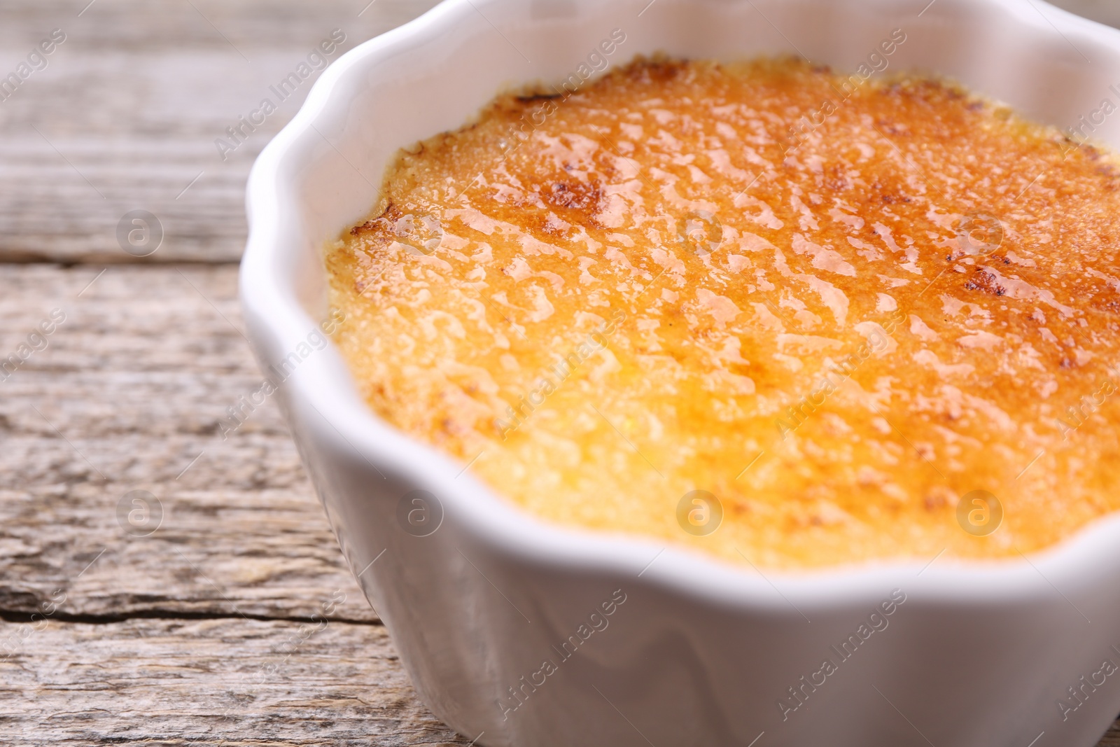 Photo of Delicious creme brulee in bowl on wooden table, closeup