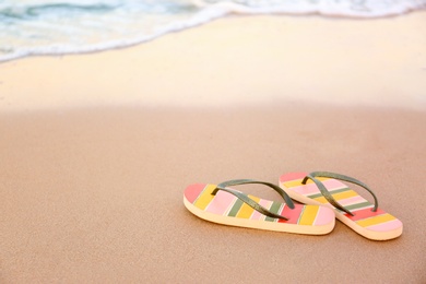 Photo of Stylish flip flops on sand near sea, space for text. Beach accessories