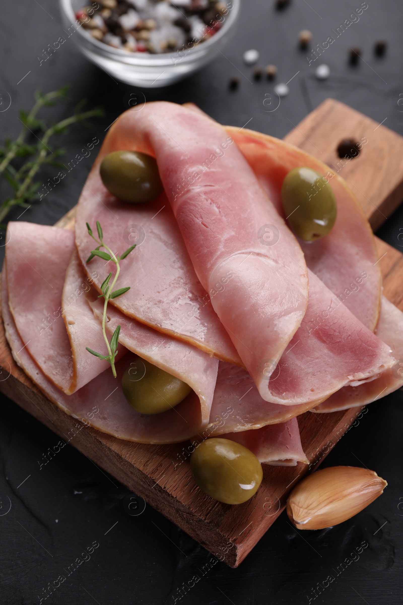 Photo of Tasty ham with olives, garlic and thyme on black textured table, closeup