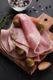 Tasty ham with olives, garlic and thyme on black textured table, closeup