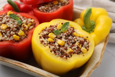 Photo of Quinoa stuffed bell peppers and basil in baking dish on white table, closeup