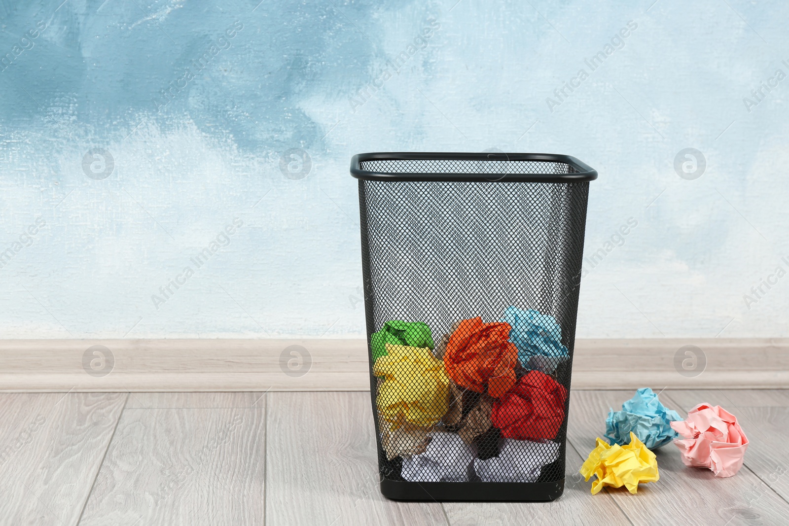 Photo of Basket with crumpled paper near light blue wall. Space for text