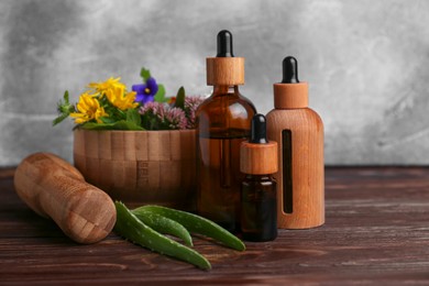 Photo of Glass bottles of aromatic essential oil and mortar with different herbs on wooden table