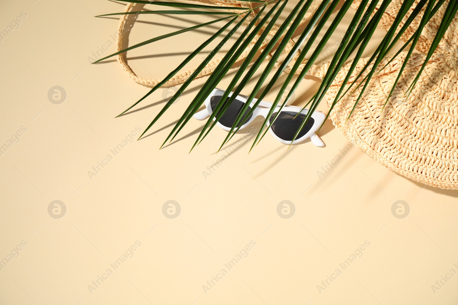 Photo of Straw bag, sunglasses and tropical leaf on beige background, flat lay. Space for text