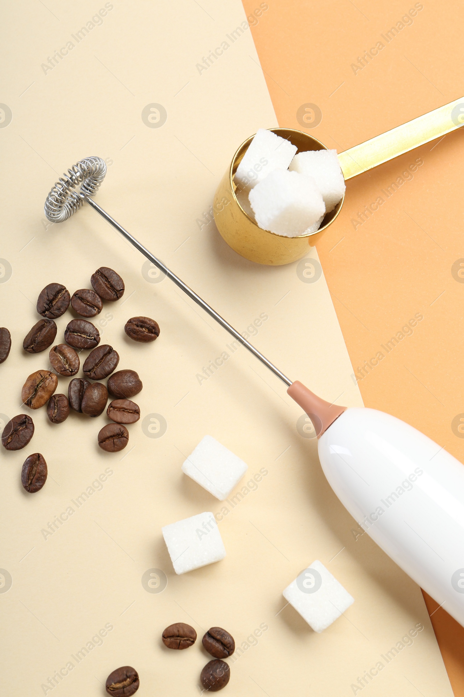 Photo of Milk frother wand, coffee beans and sugar cubes on color background, flat lay