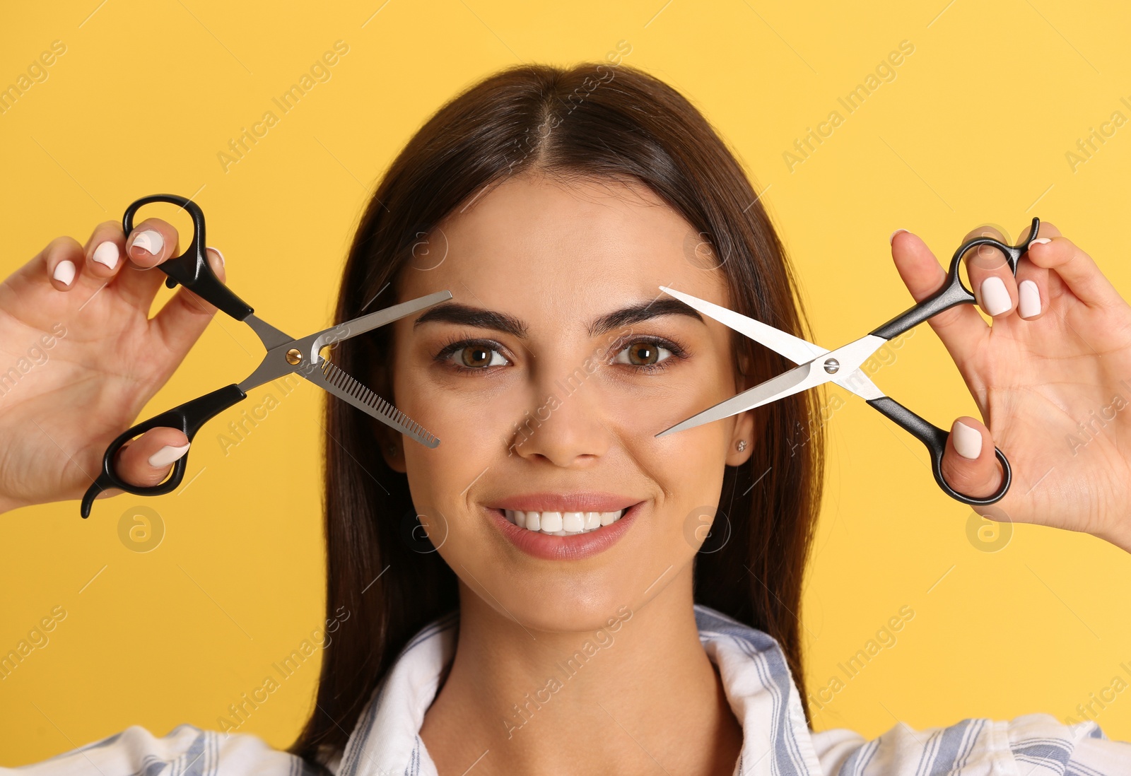 Photo of Young hairstylist holding professional scissors on color background