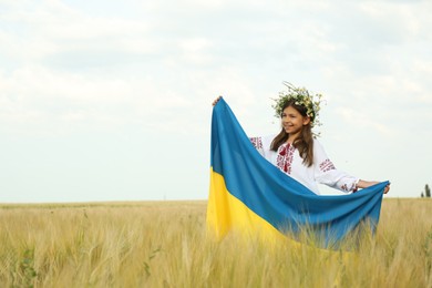Photo of Happy little girl with national flag of Ukraine in wheat field. Space for text