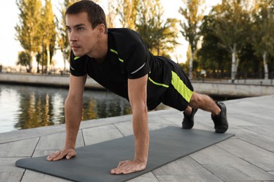 Sporty man doing straight arm plank exercise near river