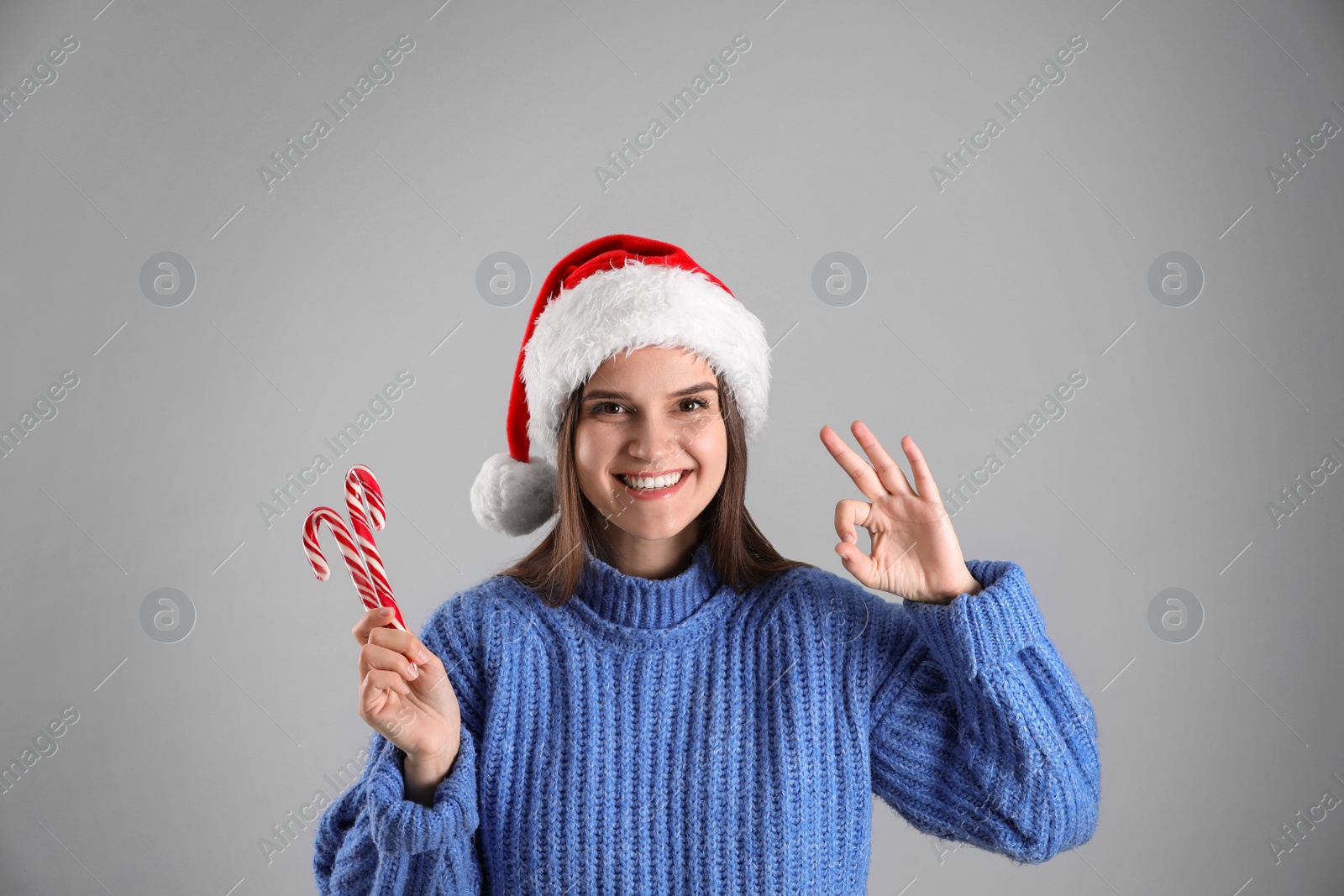 Photo of Pretty woman in Santa hat and blue sweater holding candy canes on grey background