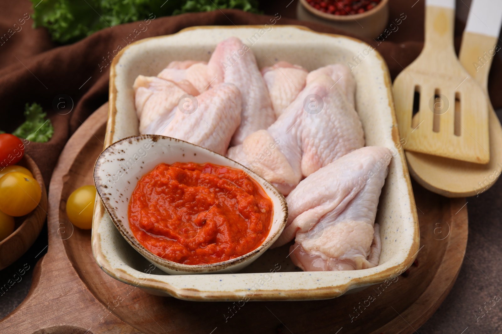 Photo of Fresh marinade, raw chicken and tomatoes on brown table, closeup