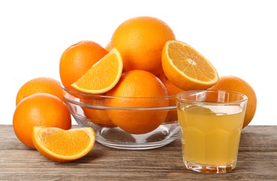 Fresh oranges in bowl and glass of juice on wooden table against white background