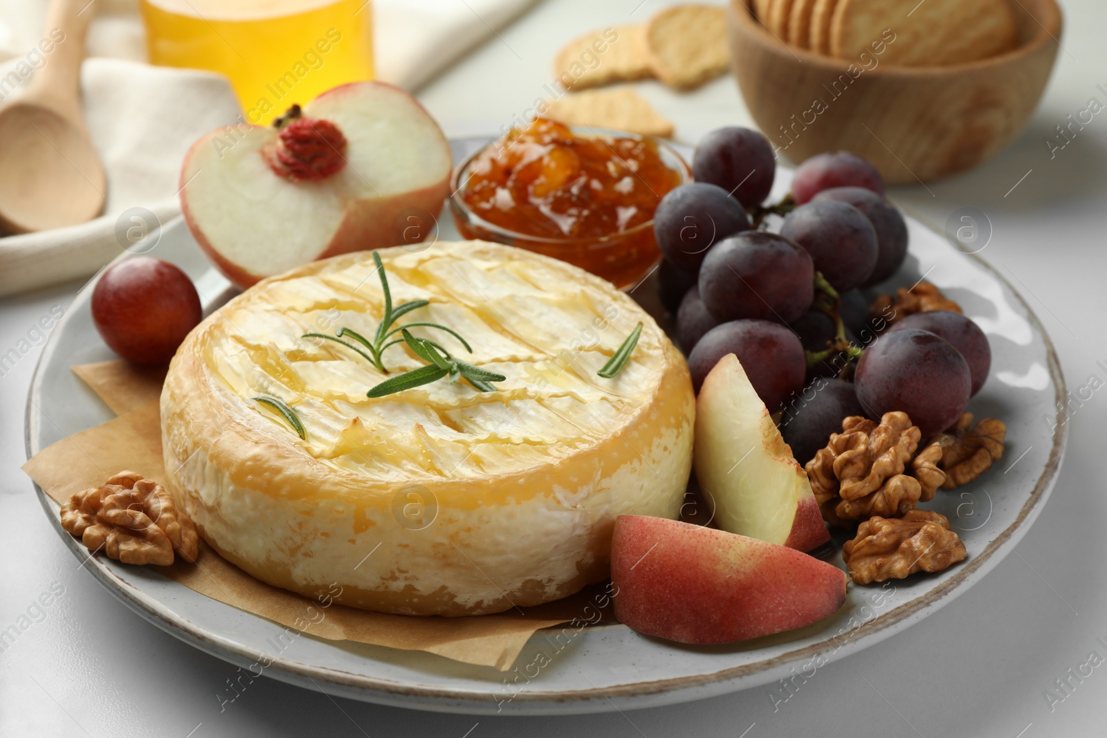 Photo of Tasty baked brie cheese with fruits, walnuts and jam on white table, closeup
