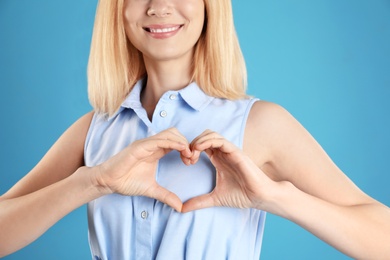 Photo of Woman making heart with her hands on color background, closeup
