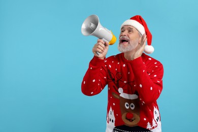 Senior man in Christmas sweater and Santa hat shouting in megaphone on light blue background. Space for text