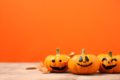 Photo of Pumpkins with scary faces and fallen leaves on orange background, space for text. Halloween decor