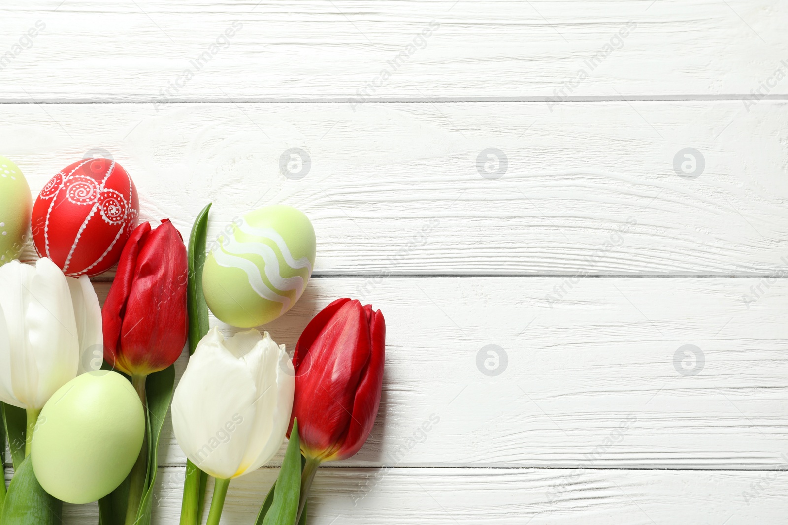 Photo of Flat lay composition of painted Easter eggs and spring flowers on wooden background, space for text