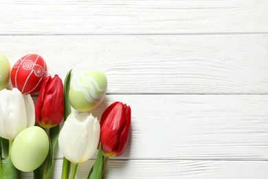 Photo of Flat lay composition of painted Easter eggs and spring flowers on wooden background, space for text