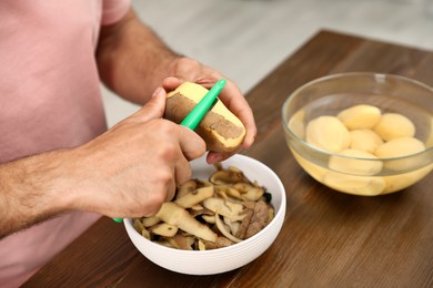 Photo of Man peeling potato at table, closeup. Preparing vegetable