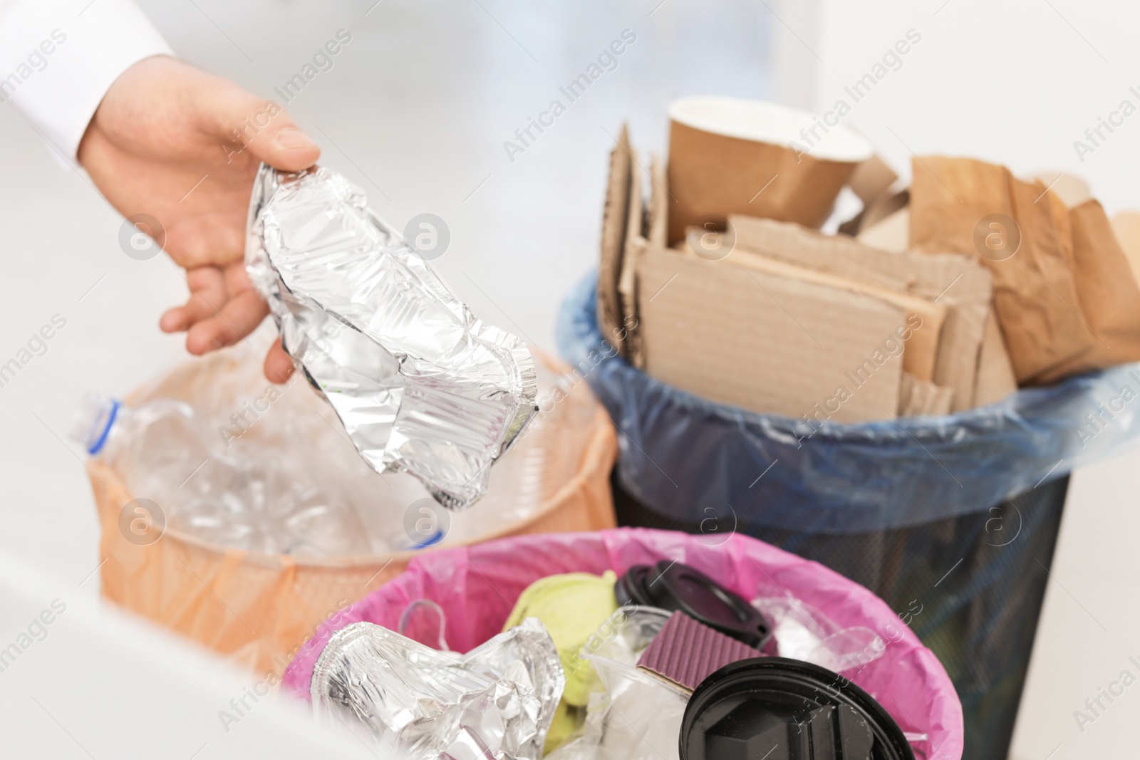 Photo of Man putting used foil container into trash bin, closeup. Waste recycling
