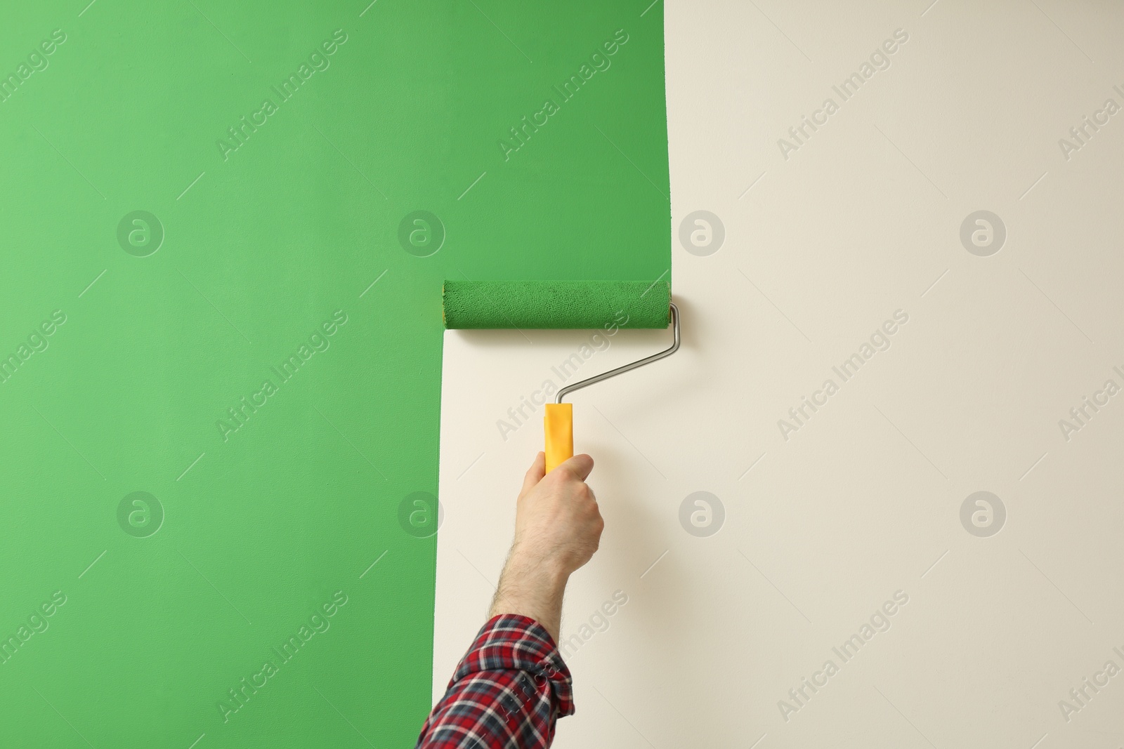 Photo of Man applying green paint with roller brush on white wall, closeup