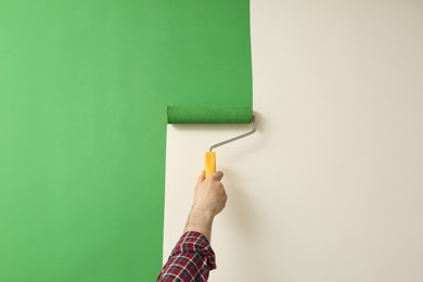 Man applying green paint with roller brush on white wall, closeup