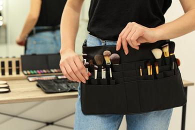 Photo of Professional makeup artist with belt organizer full of tools working in studio, closeup