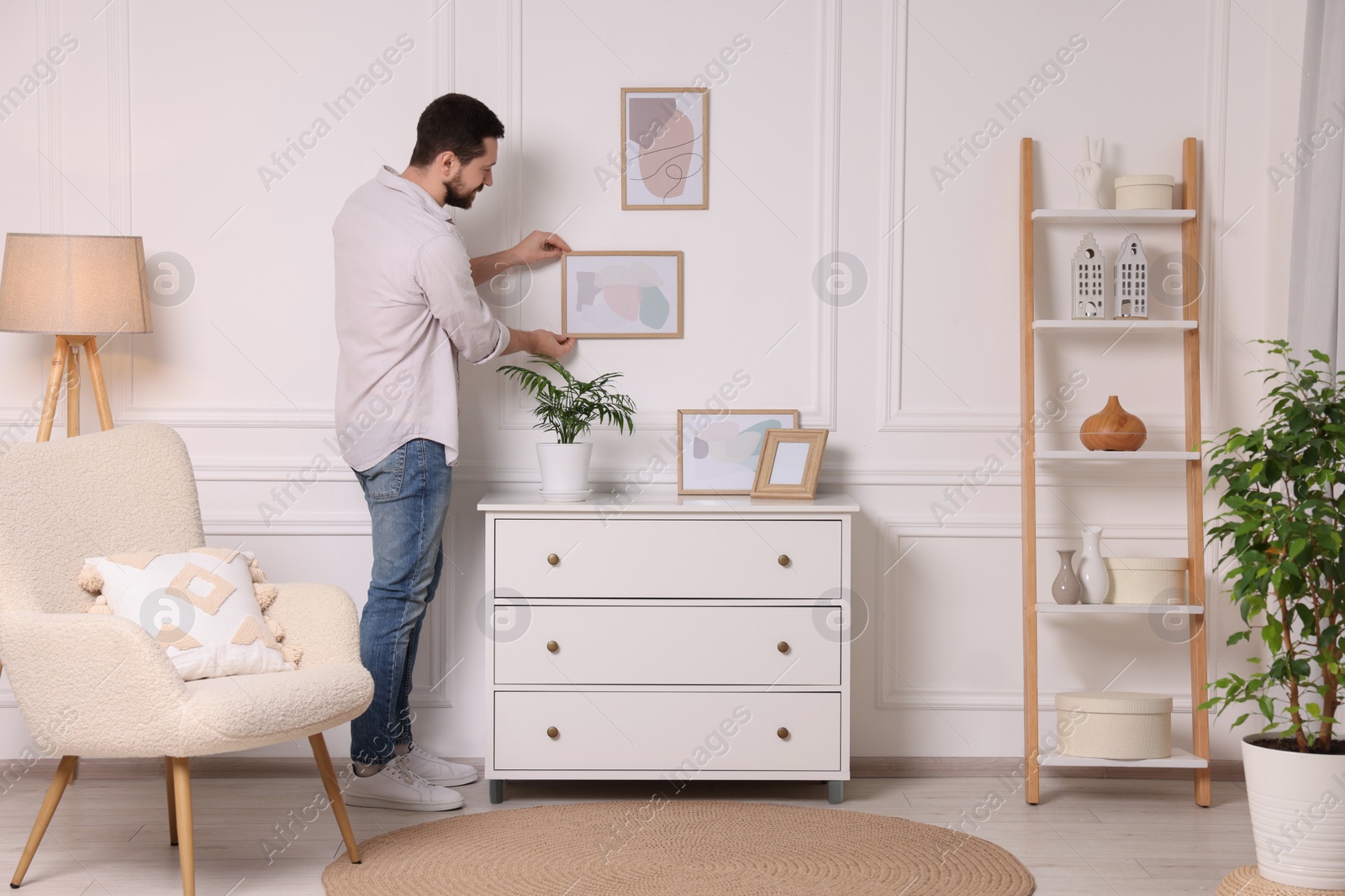 Photo of Man hanging picture frame on white wall at home