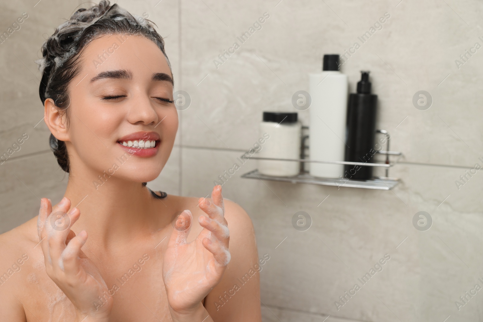 Photo of Happy woman washing hair with shampoo in shower. Space for text