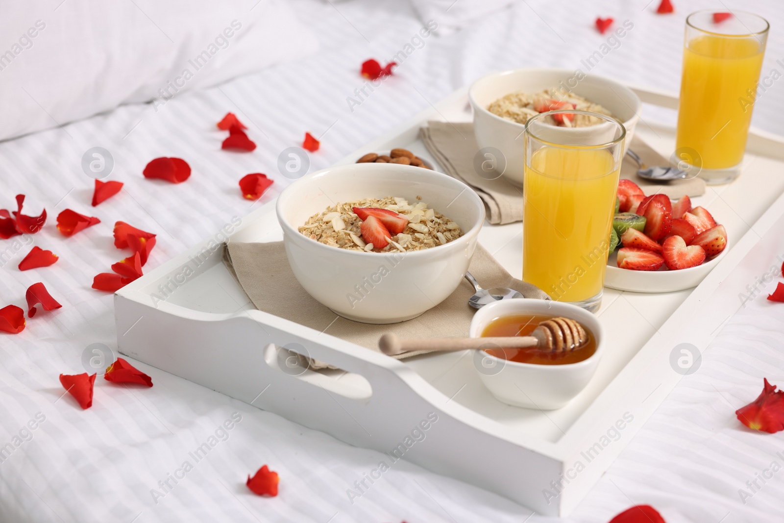 Tray with tasty breakfast and rose petals on bed at home Photo of Tray with tasty breakfast and rose petals on bed at home