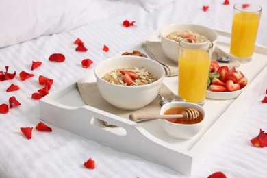 Photo of Tray with tasty breakfast and rose petals on bed at home