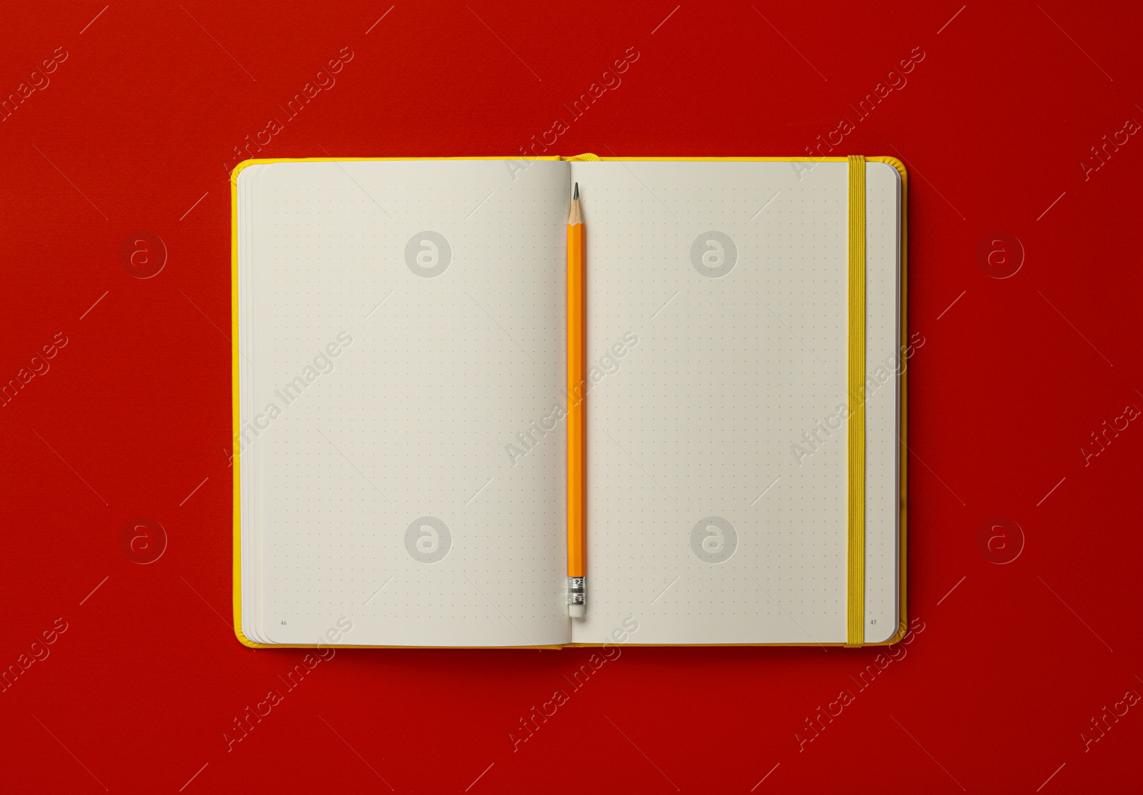 Photo of Notebook and pencil on red background, top view