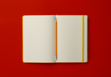 Photo of Notebook and pencil on red background, top view