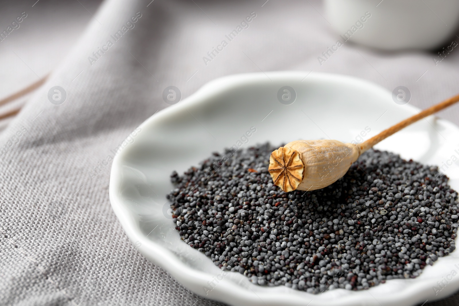 Photo of Plate with dry poppy head and seeds on fabric, closeup