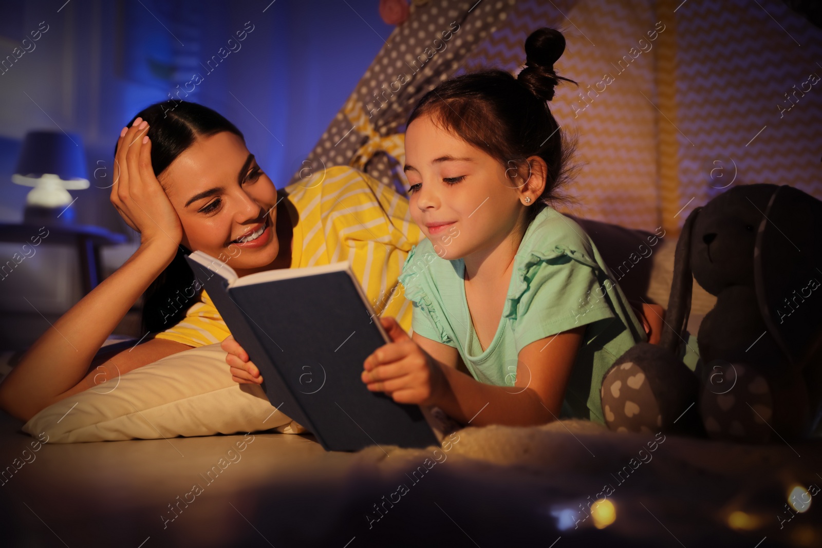 Photo of Little girl with mother reading fairy tale in play tent at home