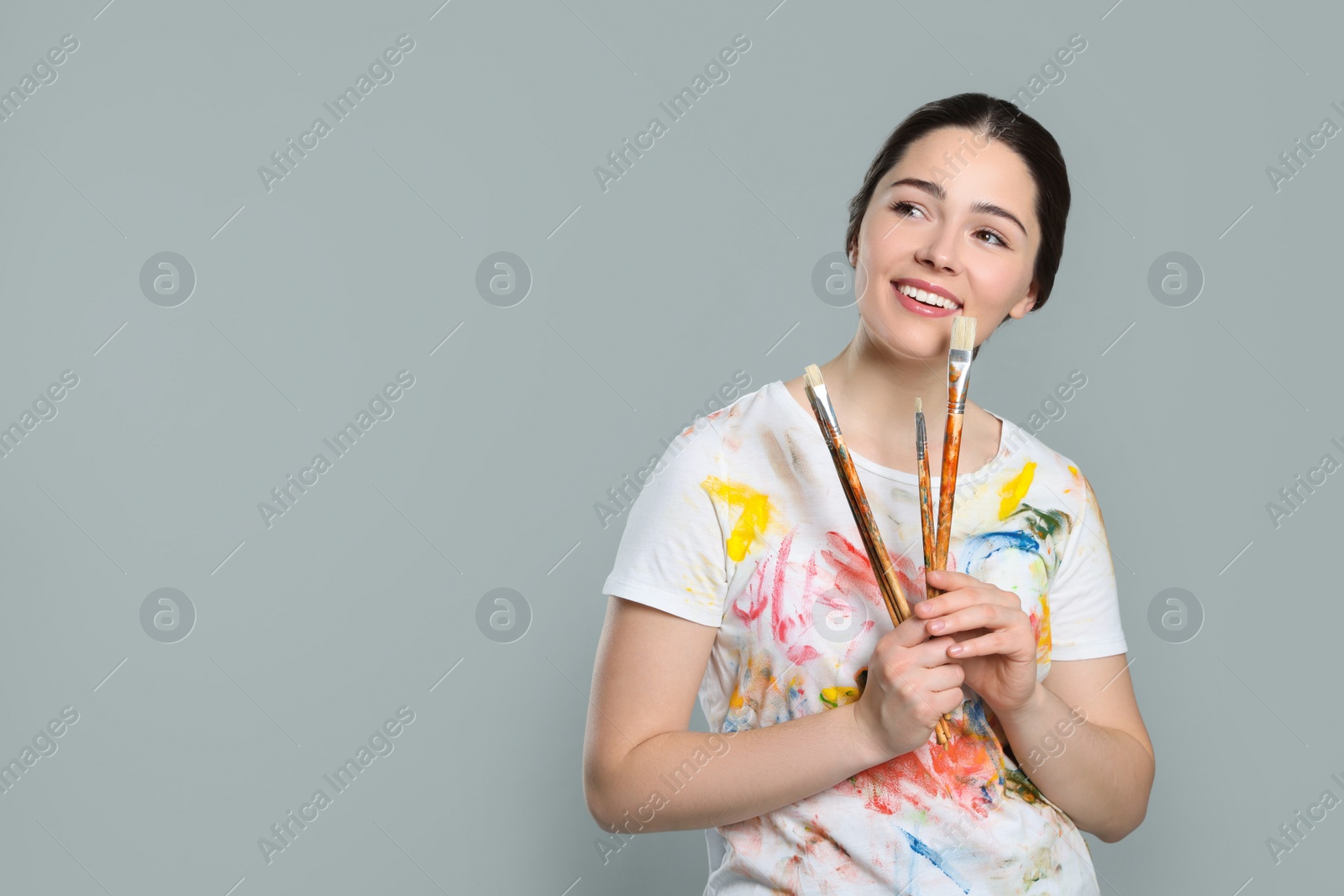 Photo of Woman with paintbrushes on grey background, space for text. Young artist