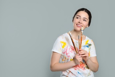 Photo of Woman with paintbrushes on grey background, space for text. Young artist