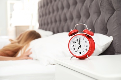 Analog alarm clock and blurred sleepy woman on background. Time of day