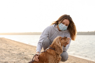 Woman in protective mask with English Cocker Spaniel on beach. Walking dog during COVID-19 pandemic