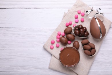 Photo of Delicious chocolate eggs, paste and candies on white wooden table, flat lay. Space for text