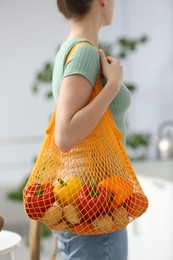 Woman with net bag full of fruits and vegetables in kitchen, closeup