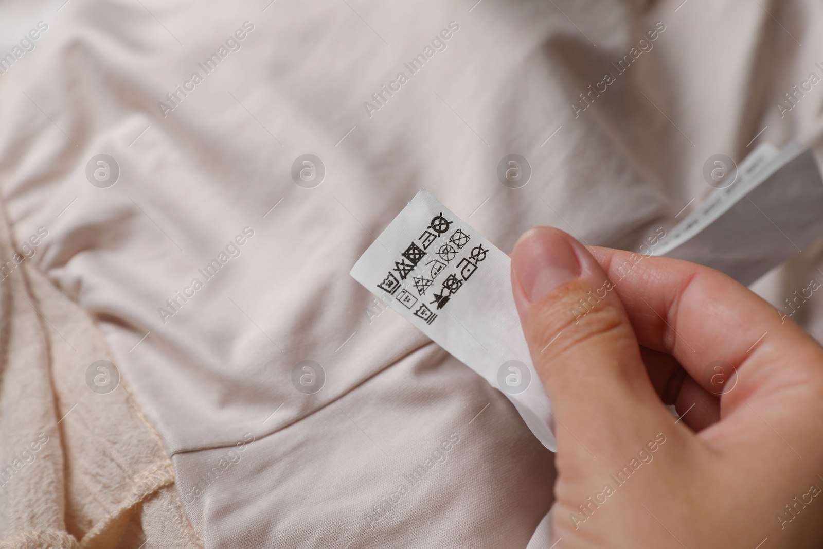 Photo of Woman holding clothing label on beige garment, closeup