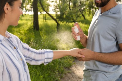 Photo of Man applying insect repellent on his girlfriend's arm in park, closeup. Tick bites prevention