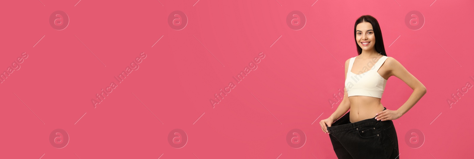 Photo of Happy young woman wearing big jeans after weight loss on pink background