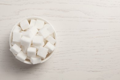 Photo of Bowl with sugar cubes on white wooden table, top view. Space for text