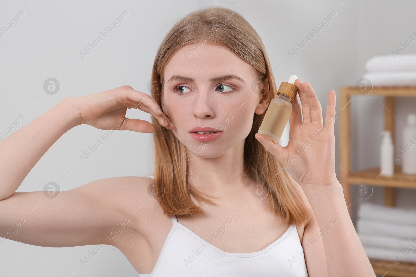 Photo of Young woman with bottle of essential oil in bathroom